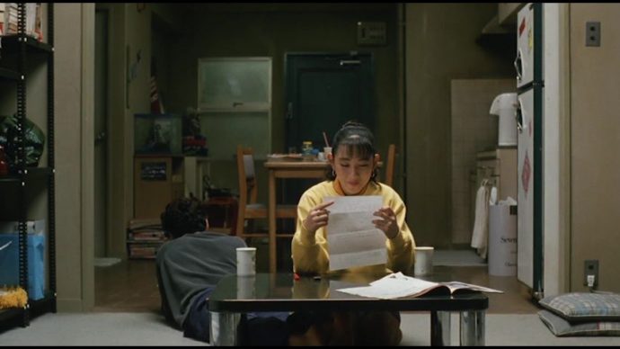 Takako, agora está em primeiro plano, sentada diante da mesa, lê o formulário de Shigaru sorrindo. Ao lado dela, Shigaru está deitado no chão de costas para a câmera.
