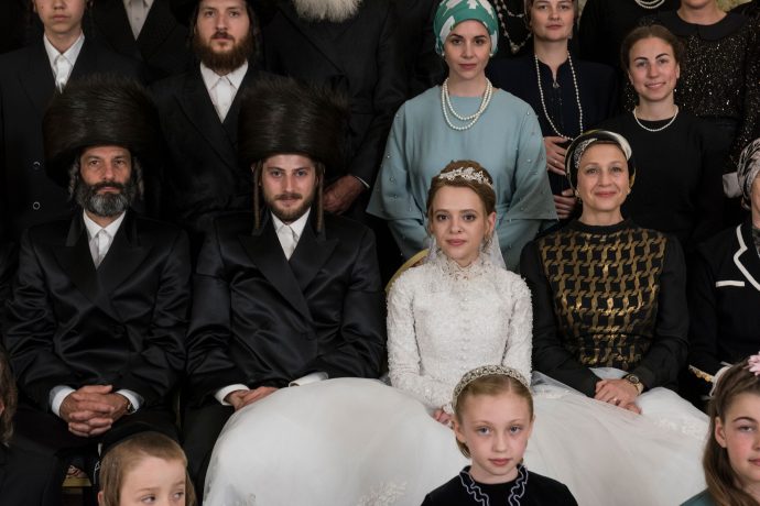 Uma criança ortodoxa vestida de noiva posa para uma foto em meio a diversos convidados 