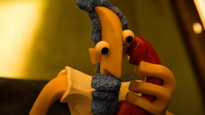 Frame do stop-motion Contra Filé de Pedro Lua. Um homem de barba azul segura um telefone vermelho em sua orelha.